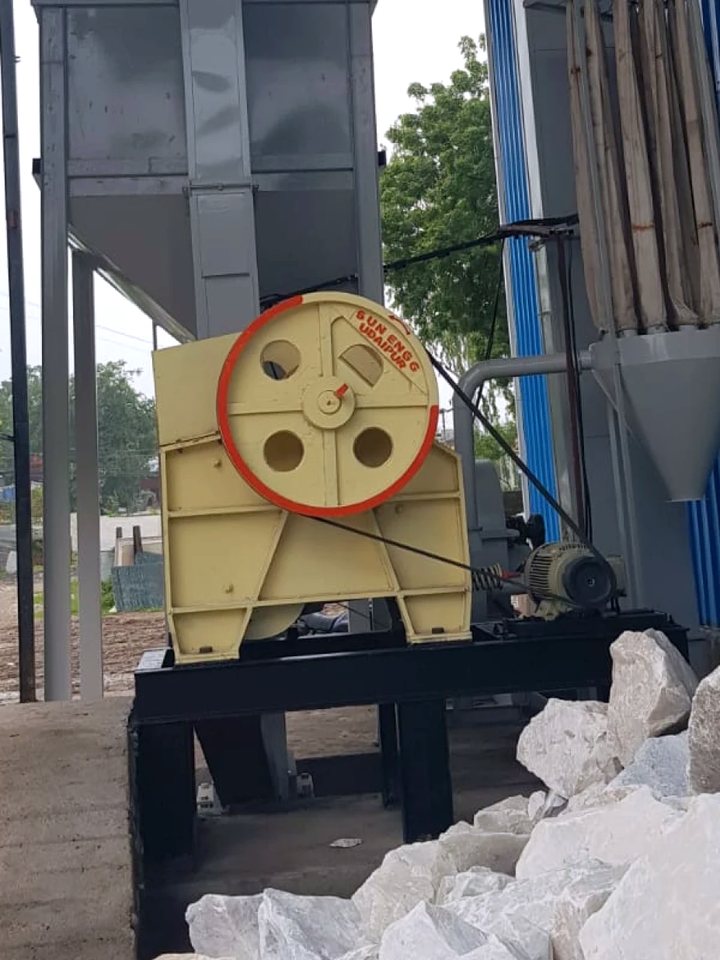 Jaw crusher in service outside a works, with broken mineral rock stacked beside the feed